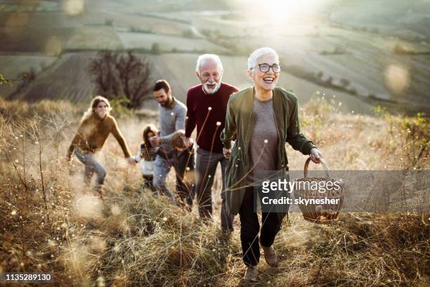 femme âgée heureuse menant sa famille à la place parfaite de pique-niquer sur la colline. - vitality photos et images de collection