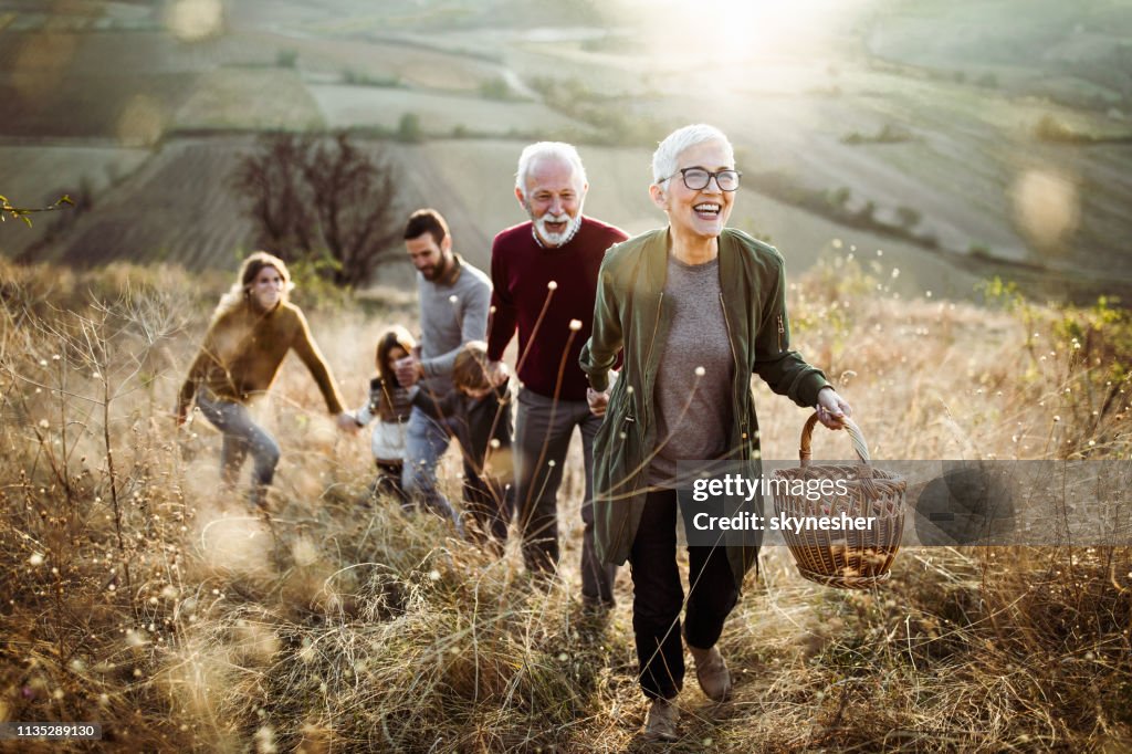 Happy senior woman leading her family to perfect picnic place on the hill.