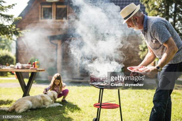 uomo maturo che prepara il barbecue per suo nipote nel cortile di casa. l'attenzione è rivolta all'uomo. - sausage sizzle foto e immagini stock