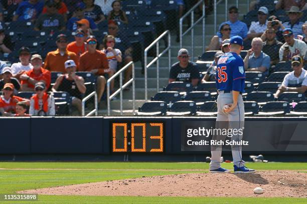 Pitcher Jacob Rhame of the New York Mets gets set to deliver a pitch as the pitch clock counts down during the ninth inning of a spring training...