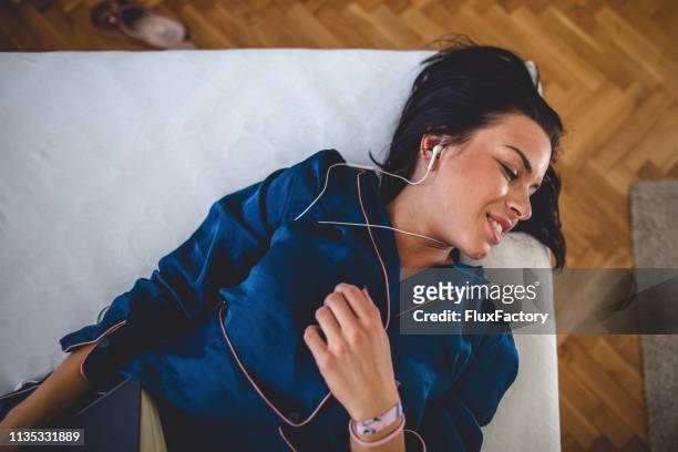 serene young woman lying in bed enjoying the music - silk pajamas stock pictures, royalty-free photos & images
