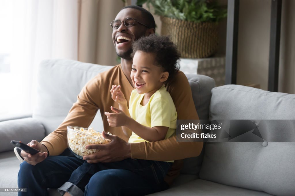 Happy african dad and kid son laughing watching funny comedy
