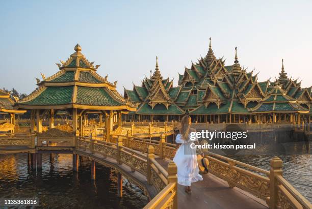 woman in long white dress walking on a bridge in a buddhist temple in thailand during sunset . - bangkok stock-fotos und bilder
