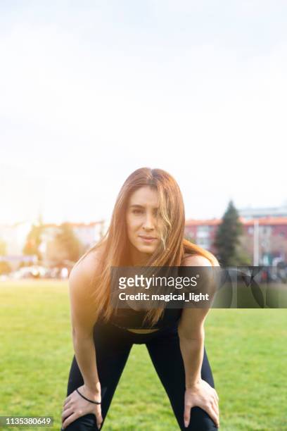 young athletic woman taking a break from training standing resting her hands on her knees on a rural track through lush farmland in a health and fitness concept – image - standing with hands on knees imagens e fotografias de stock