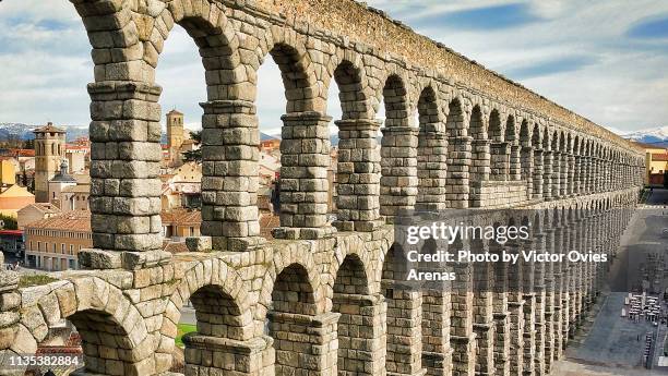 side view of the roman aqueduct (or aqueduct bridge) with the old city in the background in segovia, spain - segovia stock pictures, royalty-free photos & images