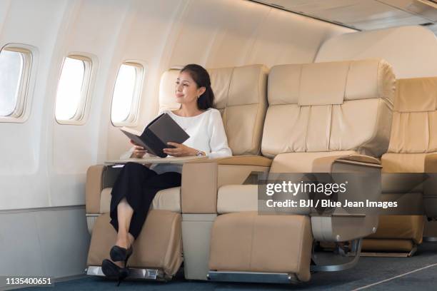 elegant mature woman reading book on airplane - vehicle seat foto e immagini stock