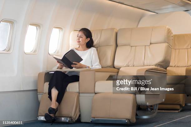 elegant mature woman reading book on airplane - vehicle seat stock pictures, royalty-free photos & images
