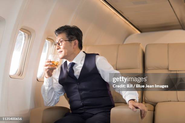 senior businessman drinking whiskey on airplane - wealthy asian man stock pictures, royalty-free photos & images