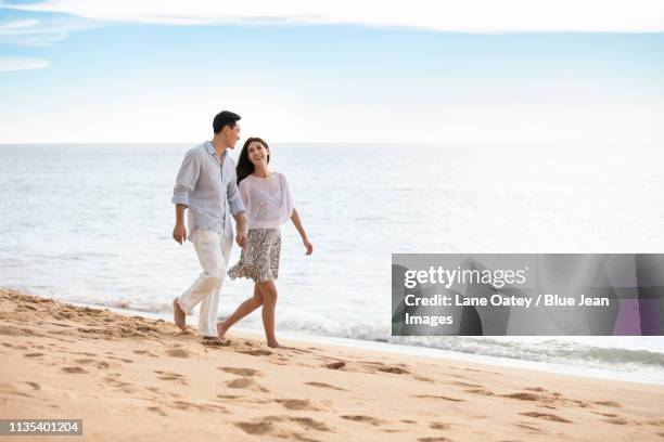 happy young couple walking on beach - asian man barefoot foto e immagini stock