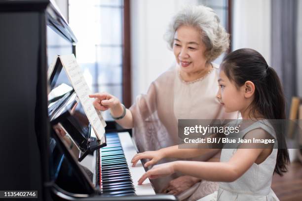 grandmother teaching granddaughter to play the piano - fabolous musician stockfoto's en -beelden