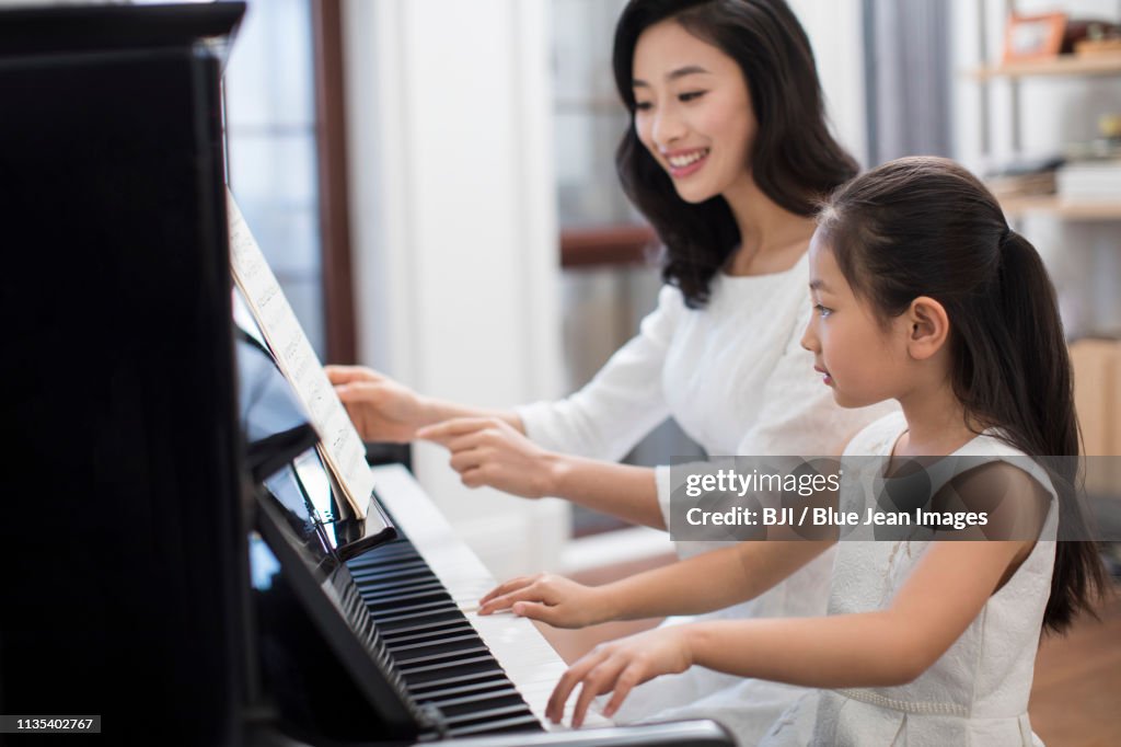 Mother teaching daughter to play the piano