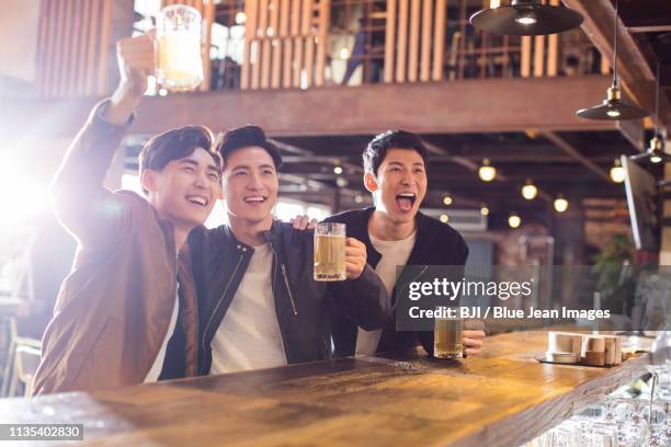 happy young men drinking beer and cheering in bar - man sipping beer smiling stockfoto's en -beelden