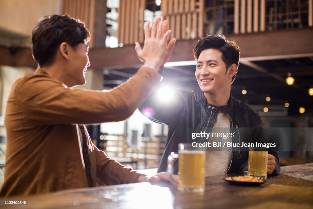 Happy young men doing high five in bar
