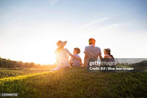 happy young family sitting on meadow - asian woman smiling sunrise stock-fotos und bilder