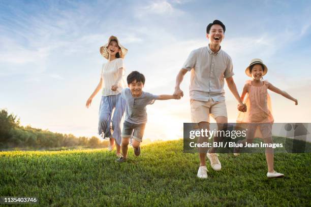 happy young family running on meadow - asian woman smiling sunrise stock-fotos und bilder