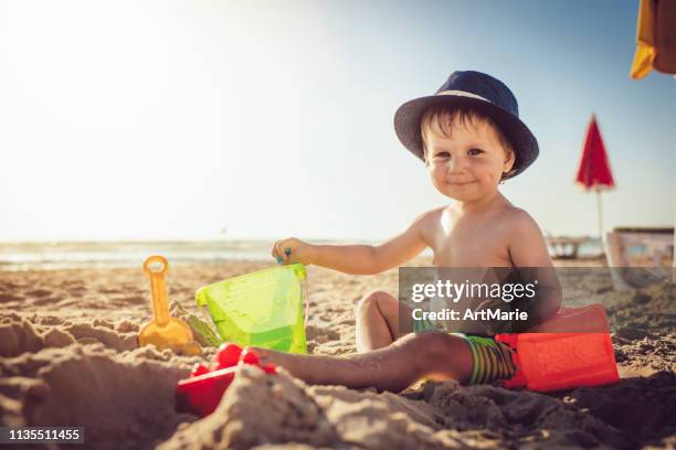 kleiner junge sitzt am strand und baut eine sandburg - kind sandburg stock-fotos und bilder