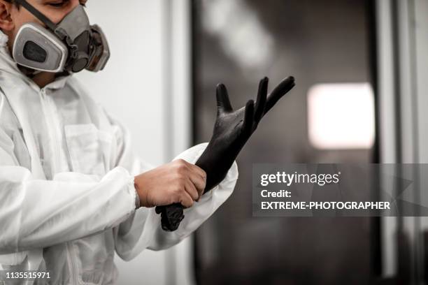 car technician getting ready for a paint job, putting on his rubber gloves in a painting chamber of a car body shop - spray booth stock pictures, royalty-free photos & images