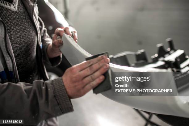 técnico de reparação de automóveis usando um papel de lixa para remover o excesso de preenchimento formam um amortecedor de carro que ficou danificado em acidente - bumper - fotografias e filmes do acervo