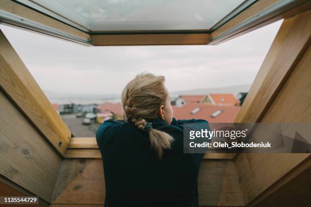 vrouw op zoek naar onze van het raam op de stad - raam stockfoto's en -beelden