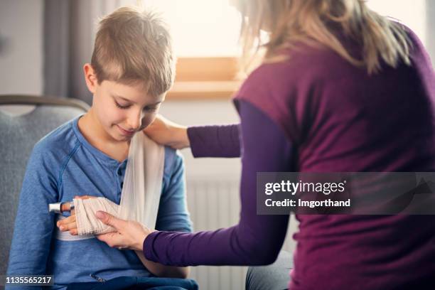 moeder neigt naar de gewonde arm van haar zoon - wounded stockfoto's en -beelden