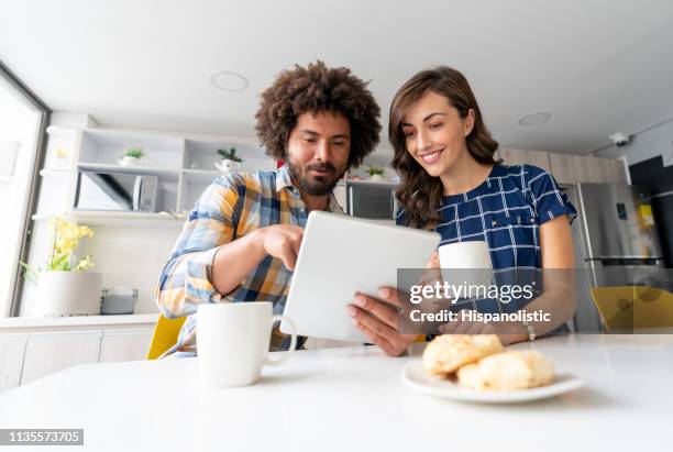 diverse partners at a coworking office in a meeting looking at a tablet while enjoying breakfast both smiling - colombia business breakfast meeting stock pictures, royalty-free photos & images
