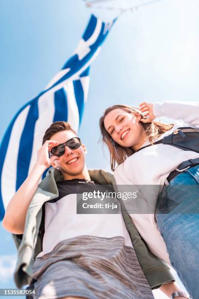 young couple standing under the greek flag - greece flag stock pictures, royalty-free photos & images