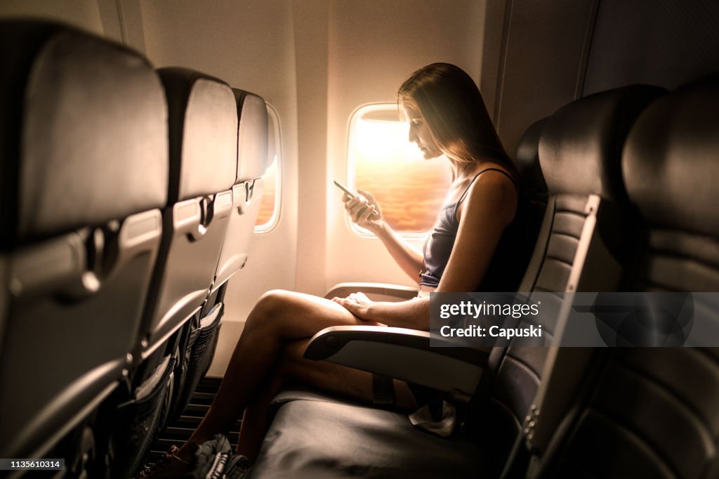 Mujer con teléfono inteligente en el asiento del avión