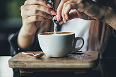 The girl's hand pours sugar into her coffee. Close up