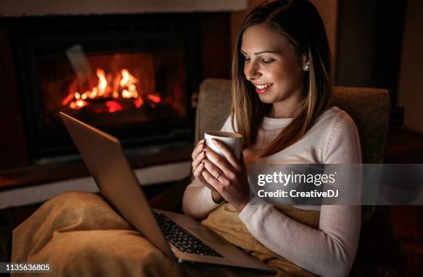 woman using laptop near fireplace - winter sofa stock pictures, royalty-free photos & images