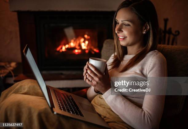 woman using laptop near fireplace - cosy fire stock pictures, royalty-free photos & images