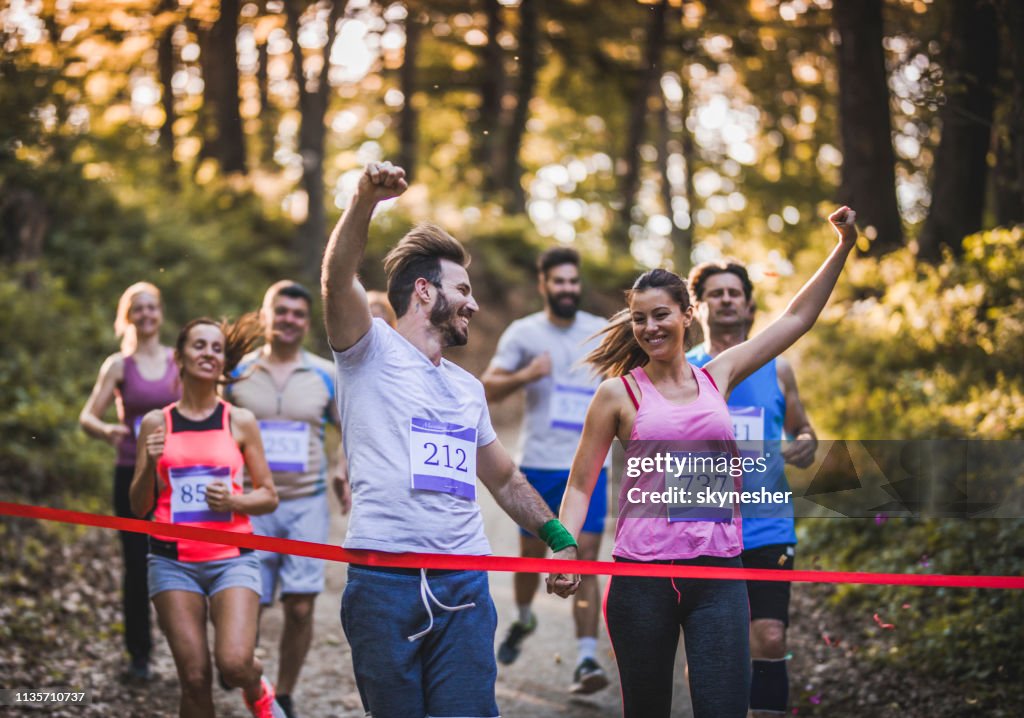 Pares alegres que ganham a raça de maratona na floresta e no cruzamento terminam a linha junto.