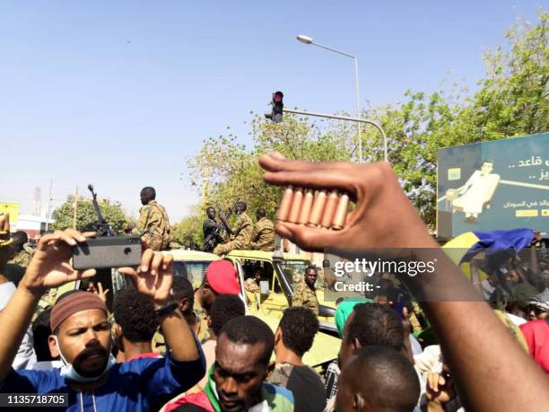 Sudanese protester shows bullet cartridges as others gather in front of security forces during a demonstration in the area of the military...