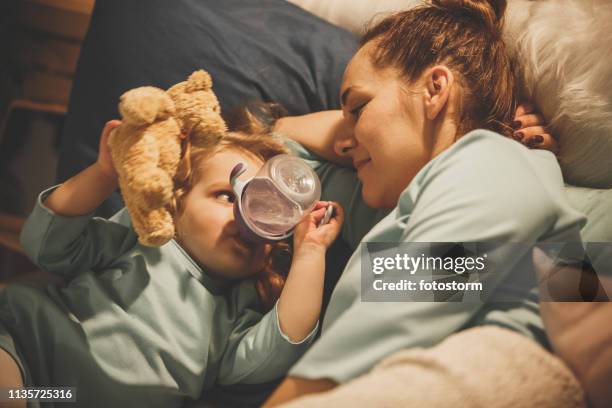 niña de dos años bebiendo agua de la botella en la cama - niño-tomando-agua fotografías e imágenes de stock