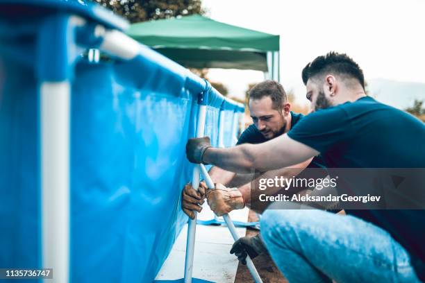 two males setting up portable pool holders - inflatable swimming pool stock pictures, royalty-free photos & images