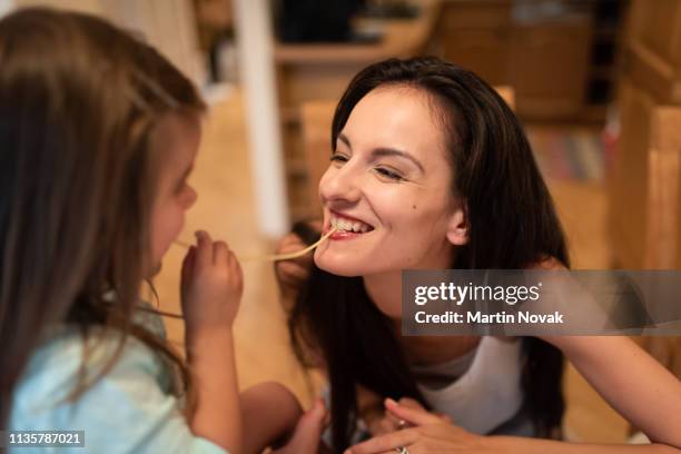 little girl sharing spaghetti strand with mom - the joys of eating spaghetti stock pictures, royalty-free photos & images