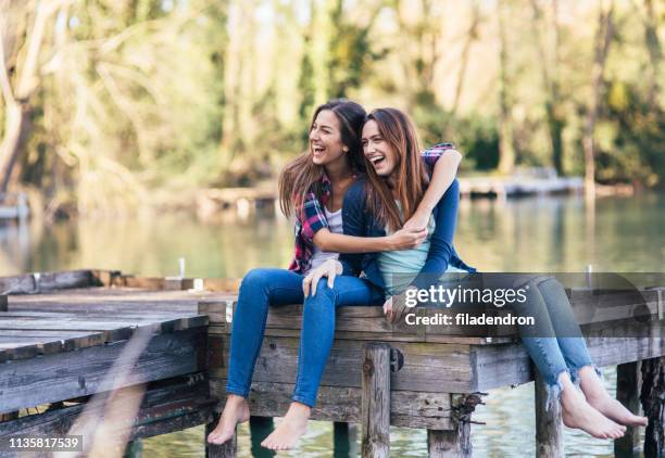 vriendinnen genieten van tijd samen in de buurt van de rivier - girls barefoot in jeans stockfoto's en -beelden