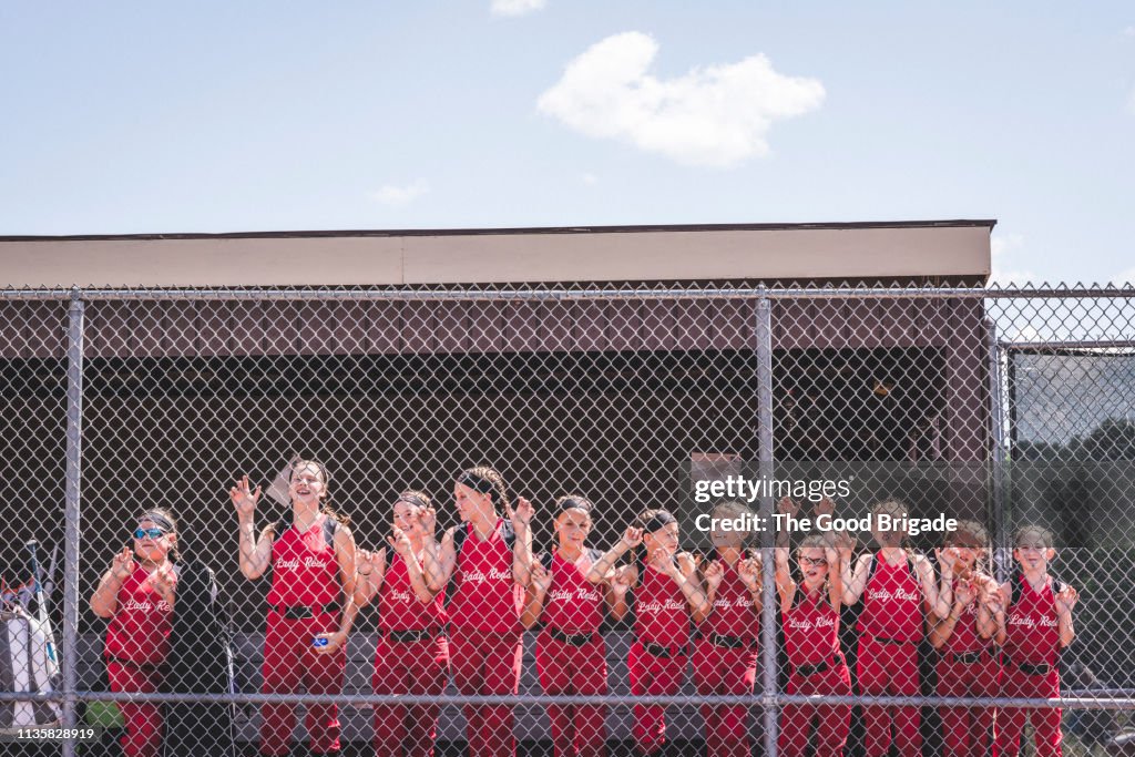 Softball team standing by fence in dugout