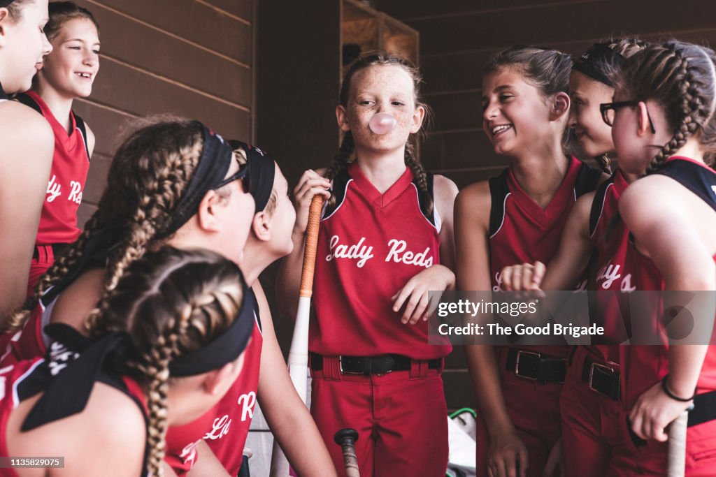 Girl blowing bubble gum in dugout during softball game
