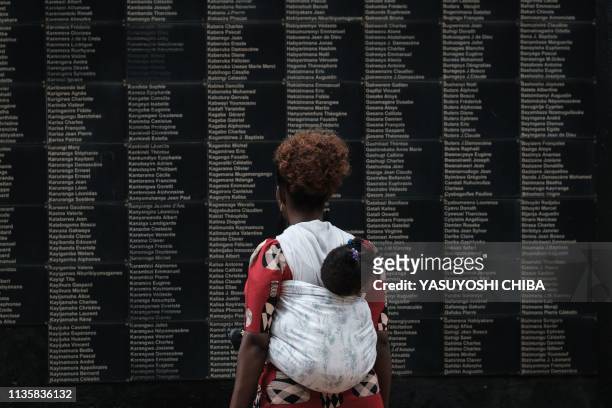 Woman carrying her child looks at the wall of victims' names as Rwanda marks the 25th Commemoration of the 1994 Genocide at the Kigali Genocide...