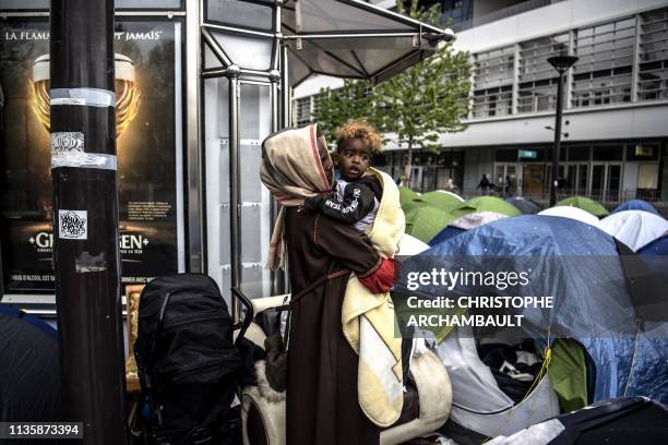 An asylum seeker holds her one-year-old son as they stand outside their a tent at a makeshift camp housing mainly families, at Porte d'Aubervilliers...