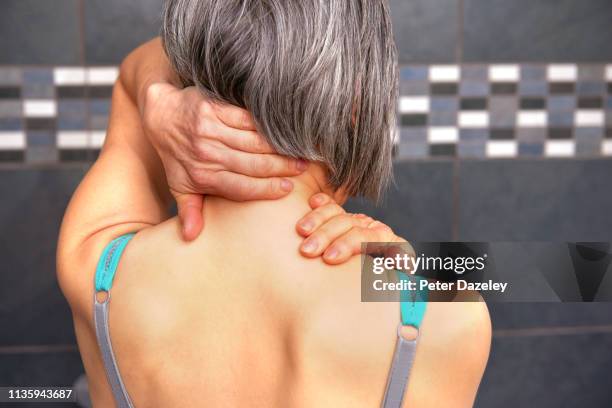 woman rubbing back of neck - arthritis stockfoto's en -beelden