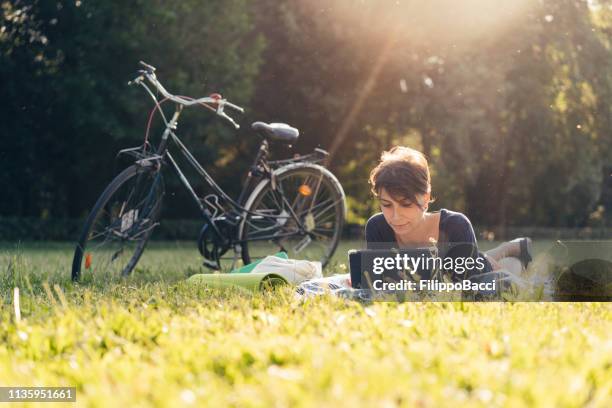 young adult woman reading an ebook at a public park - bike ipad stock pictures, royalty-free photos & images