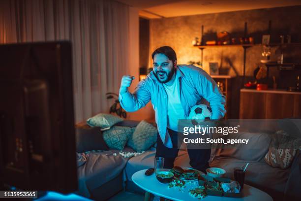 overweight guy watching a soccer match at home - spectator stock pictures, royalty-free photos & images