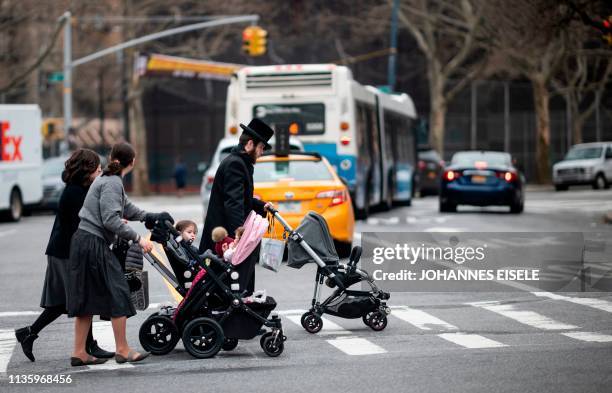 Jewish man and two woman pushes strollers as they cross a street in a Jewish quarter in Williamsburg Brooklyn on April 9, 2019 in New York City. -...