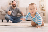 Adorable baby boy crawling on floor with dad