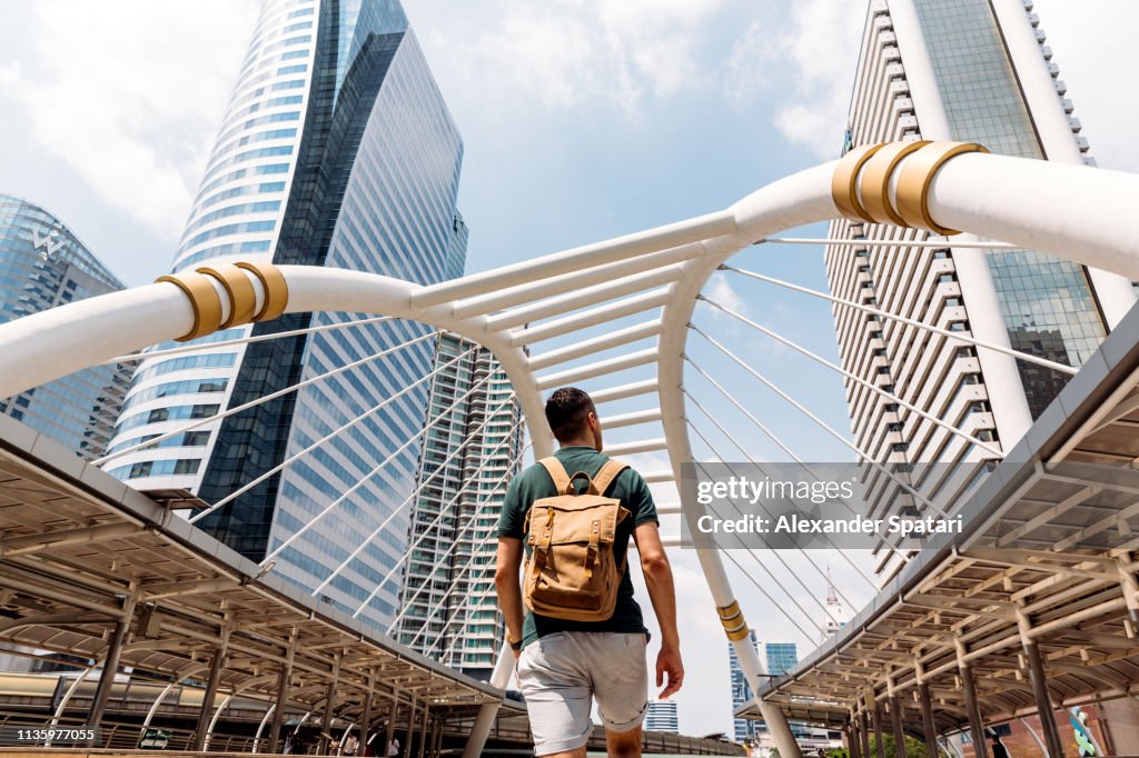 Rear view of a man with backpack admiring modern skyscrapers in Bangkok, Thailand