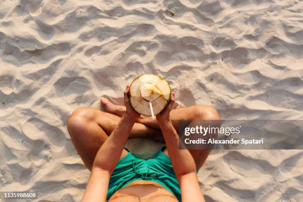 personal perspective of a young man sitting cross-legged on the beach and drinking fresh young coconut - railay strand stock pictures, royalty-free photos & images