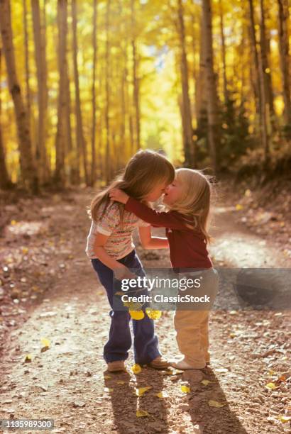 1970s TWO LITTLE GIRLS SISTERS WALKING HUGGING IN AUTUMN WOODS ON NATURE TRAIL