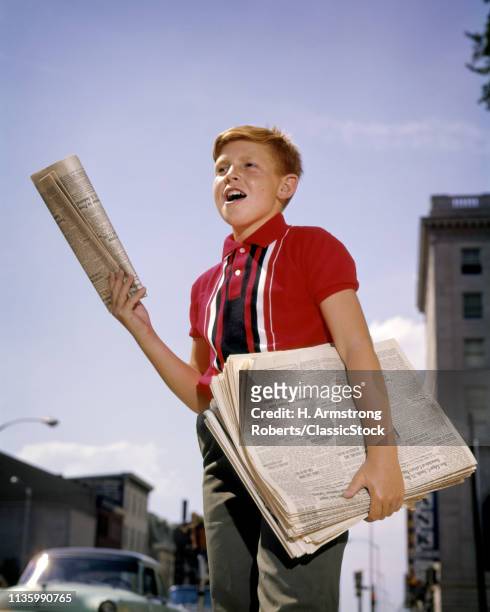 1960s NEWSBOY RED HAIR WEARING RED STRIPED SHIRT SHOUTING EXTRA EXTRA SELLING NEWSPAPERS ON CITY SIDEWALK