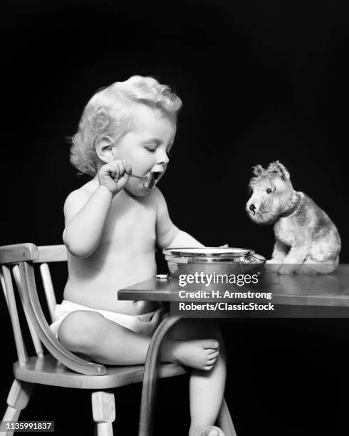 1940s CURLY BLOND HAIR BABY GIRL FEEDING HERSELF WITH SPOON WHILE STUFFED PET TOY DOG WATCHES